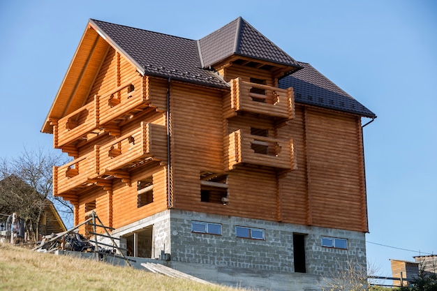 Nouvelle maison de chalet traditionnel écologique en bois de matériaux de bois naturel avec toit en bardeaux et sous-sol en pierre en construction dans un quartier vert sur l'espace de copie de ciel bleu