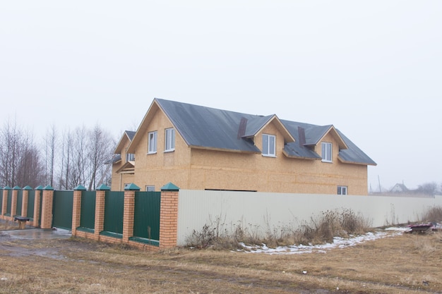 Nouvelle maison avec lucarnes clôtures de sécurité et mur sur une route rurale boueuse vue sur une froide journée d'hiver gris brumeux