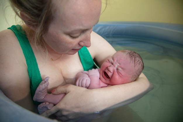 Une nouvelle mère embrassant son nouveau-né après un accouchement à domicile en piscine naturelle