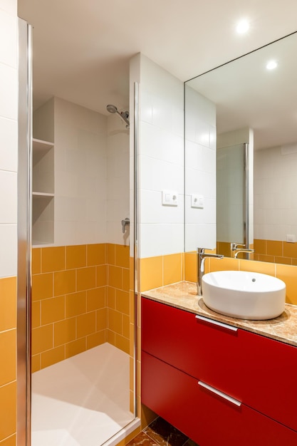 Nouvelle salle de bain vide avec douche carrelage jaune meuble rouge et miroir rectangulaire avec lavabo rond