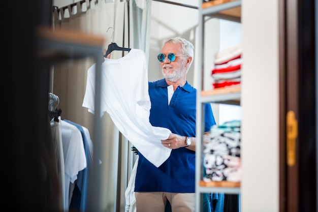 Une nouvelle tenue. Tour de taille d'un client âgé curieux scrutant un T-shirt blanc tout en le tenant à deux mains