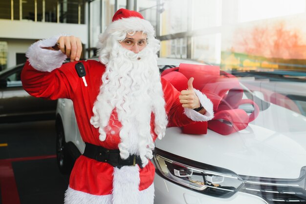 Nouvelle voiture comme cadeau de Noël. Père Noël dans la salle d'exposition de voitures près d'une nouvelle voiture.