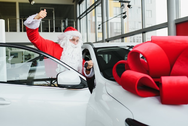 Nouvelle voiture comme cadeau de Noël. Père Noël dans la salle d'exposition de voitures près d'une nouvelle voiture.