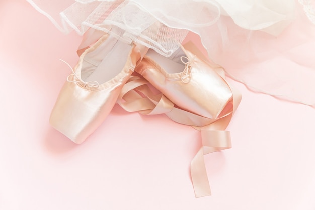 Nouvelles chaussures de ballet beige pastel avec ruban de satin et jupe tutut isolé sur table rose