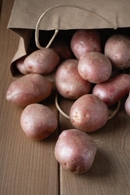 Nouvelles pommes de terre rouges crues dans un sac en papier sur fond de bois