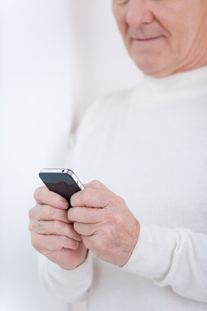 Les nouvelles technologies ne sont pas un problème pour moi. Close-up of senior man holding mobile phone tout en se penchant sur le mur