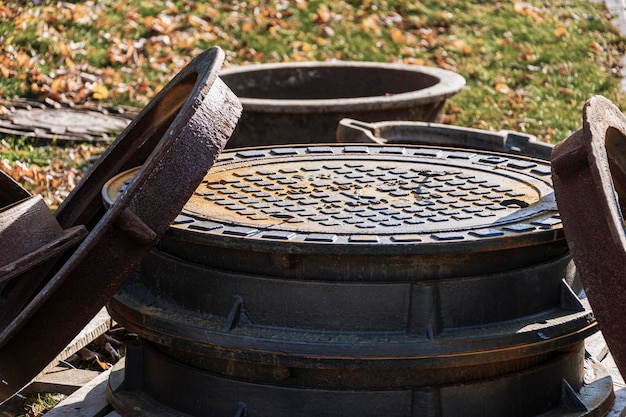 Nouvelles Trappes En Fonte Préparées Pour L'installation Sur Le Chantier. Des Trappes Avec Couvercles Reposent Sur Le Sol Sur Fond De Feuilles D'automne Tombées.