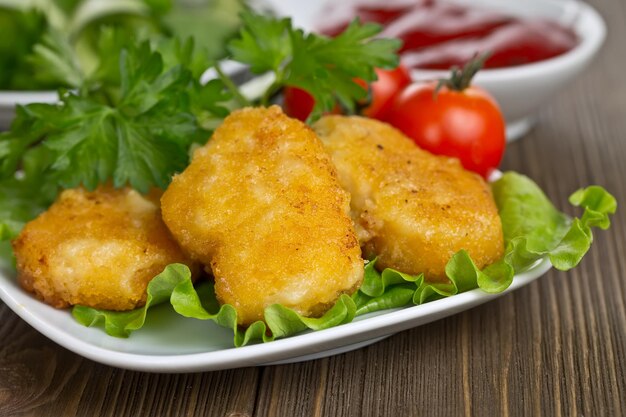 Nuggets de poulet appétissants avec des feuilles de laitue, de la laitue et des tomates en arrière-plan