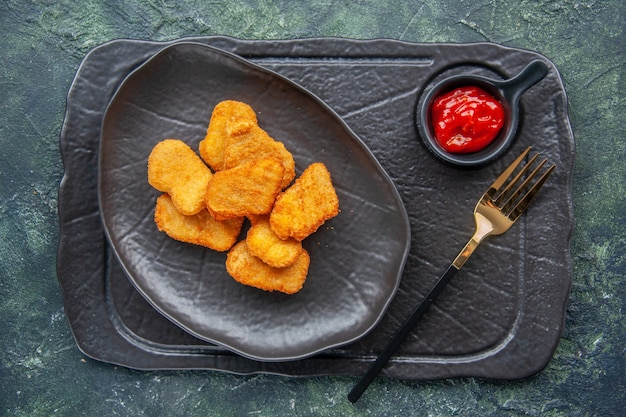 Nuggets de poulet sur une assiette noire et fourchette de ketchup sur un plateau de couleur sombre sur une surface sombre