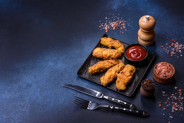 Nuggets de poulet croustillants frits avec du ketchup sur plaque noire sur fond sombre