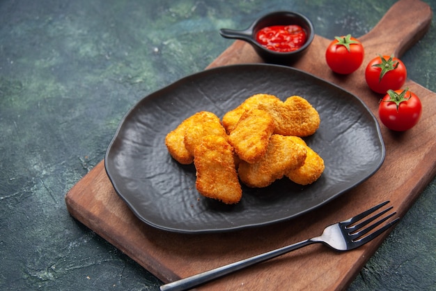 Nuggets de poulet sur une plaque noire et une fourchette sur une planche de bois ketchup de tomates sur une surface sombre avec un espace libre gros plan