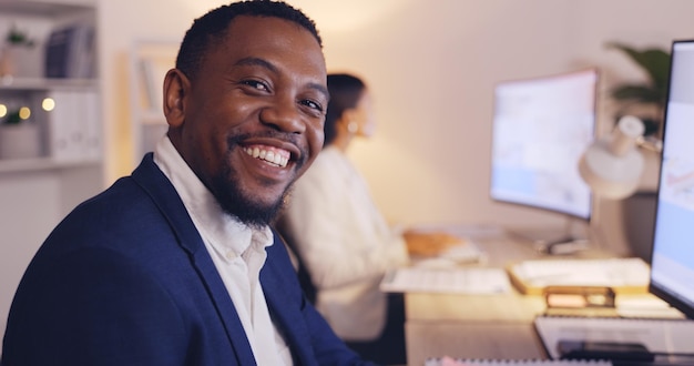 Photo nuit d'affaires et visage d'un homme noir heureux au bureau travaillant tard sur ordinateur pour planifier des objectifs et un projet directeur d'entreprise et portrait d'un entrepreneur masculin avec confiance, fierté et sourire