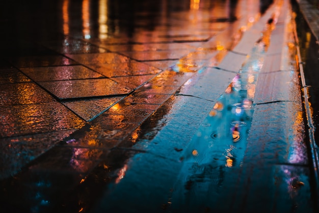 Photo nuit pluvieuse dans une grande ville, reflets de lumières sur la chaussée mouillée.