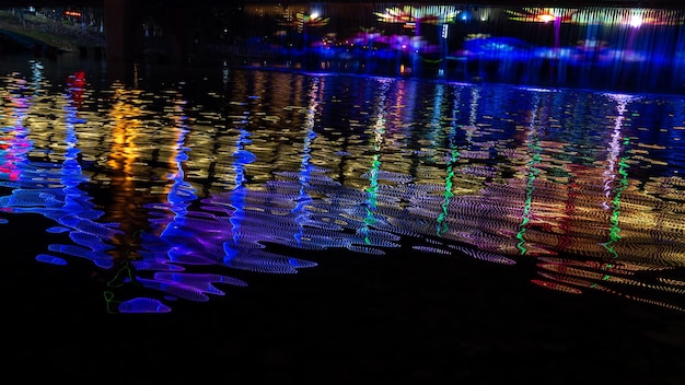 Photo la nuit, le ruisseau reflète les lumières colorées du pont.