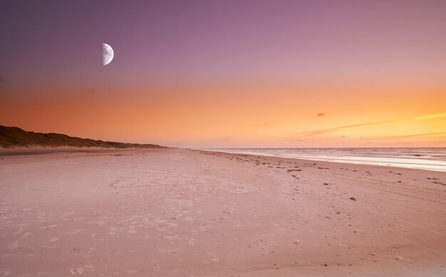 La nuit tombe sur une plage désolée La lune se lève sur une plage désolée alors que le soleil se couche sur l'océan