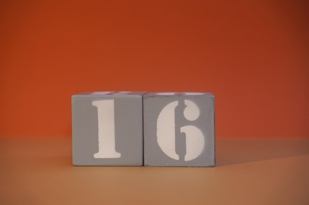 Numéro 16 sur des cubes gris en bois gros plan Concept de date heure Concept mathématique Espace de copie pour le texte ou l'événement Numéros blancs 16 sur les blocs de construction fond orange Cubes éducatifs Mise au point sélective