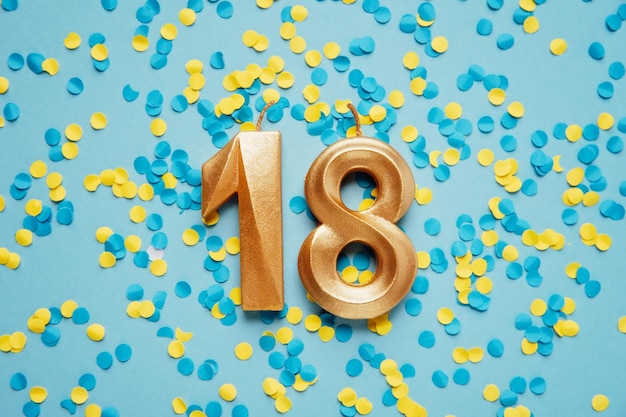 Photo numéro 18 dix-huit bougies d'anniversaire de célébration dorées sur fond de confettis jaunes et bleus