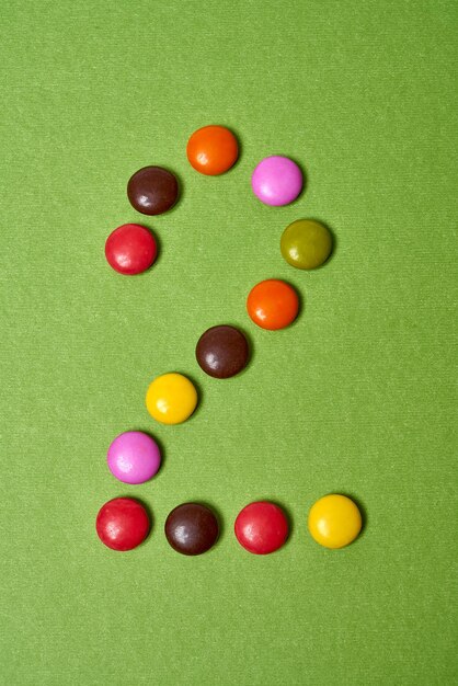 Numéro 2 écrit avec des bonbons au chocolat ronds colorés sur fond vert.