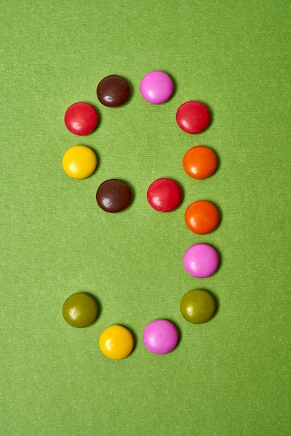 Numéro 9 écrit avec des bonbons au chocolat ronds colorés sur fond vert.