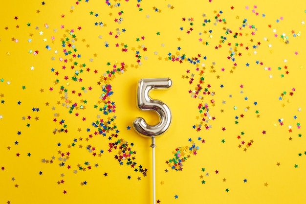 numéro cinq avec des confettis multicolores sur une surface jaune