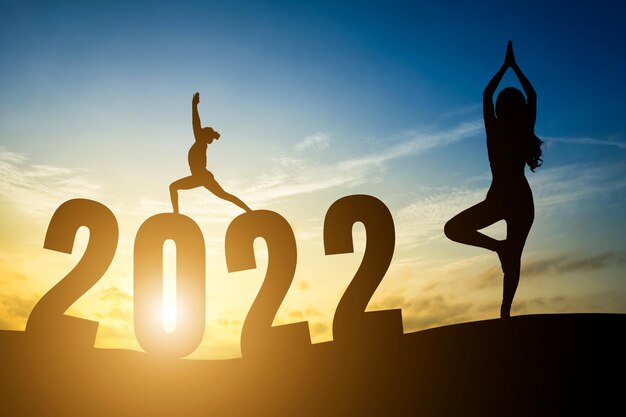 Numéros de bonne année 2022, Silhouette femme pratiquant le yoga lever du soleil tôt le matin sur l'arrière-plan de l'horizon, concept de santé et de bonne année.