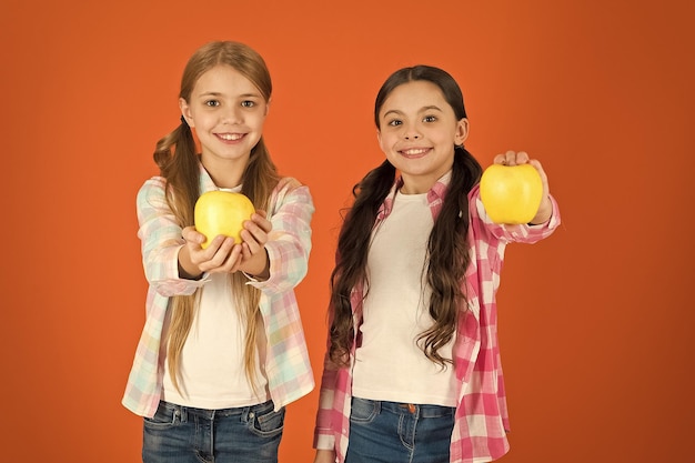 Nutrition de fruits vitaminés pour les enfants Mode de vie sain Distribution gratuite de fruits frais à l'école Les filles enfants style décontracté mangent des pommes fruits fond orange Les écolières mangent des pommes