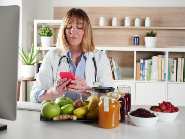 Photo nutritionniste féminine distraite discutant avec un smartphone dans un studio de bureau