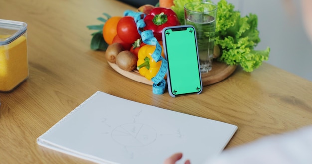 Nutritionniste parlant sur le chat vidéo à l'aide d'un smartphone avec écran vert au travail consultation en ligne Professionnel de la santé répondant à l'appel donnant une consultation à distance et rédigeant des notes de rendez-vous