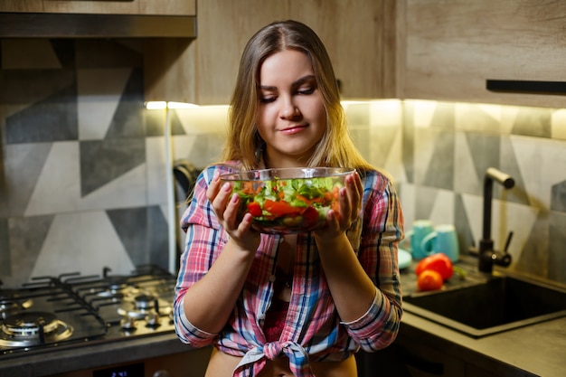 La nutritionniste végétarienne d'entraîneur de fitness prépare une salade de légumes frais dans la cuisine. Regarder sa silhouette