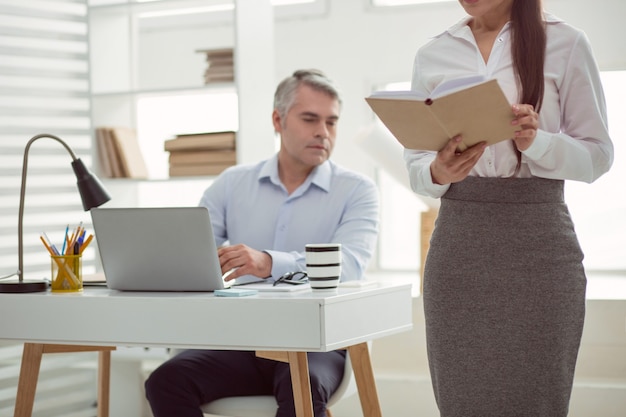 Photo objet sexuel. mise au point sélective d'une jolie femme debout au bureau et lisant le livre tout en étant l'objet d'intérêt sexuel