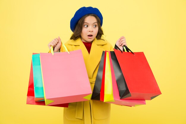 Obsédé par le shopping Fille mignonne enfant tenant des sacs à provisions sur fond jaune Vente de mi-saison Boutique avec carte de réduction Obtenez des achats à prix réduit pour l'anniversaire ou les vacances Fashionista adore faire du shopping