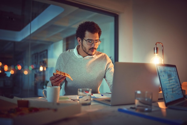 Obtenir de l'énergie pour une autre fin de soirée Photo d'un jeune designer mangeant une pizza tout en travaillant tard dans un bureau
