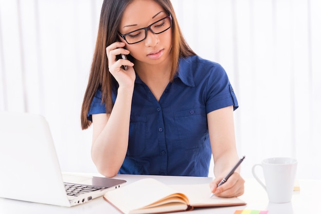 Occupé par le travail. Belle jeune femme asiatique écrit quelque chose dans son bloc-notes