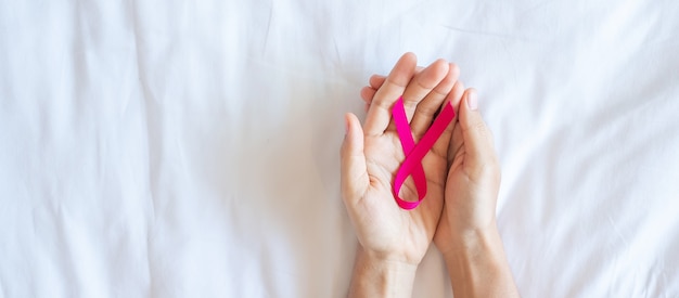 Octobre Mois de sensibilisation au cancer du sein, main de femme adulte tenant un ruban rose sur fond rose pour soutenir les personnes vivant et malades. Concept de la journée internationale des femmes, des mères et du monde contre le cancer