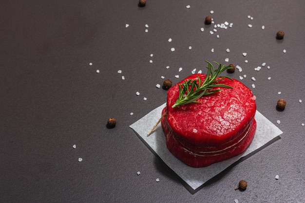 Oeil cru de steak rond avec des épices et des herbes sur fond de béton en pierre noire Un espace de copie plat à la mode à l'ombre sombre et à la lumière dure