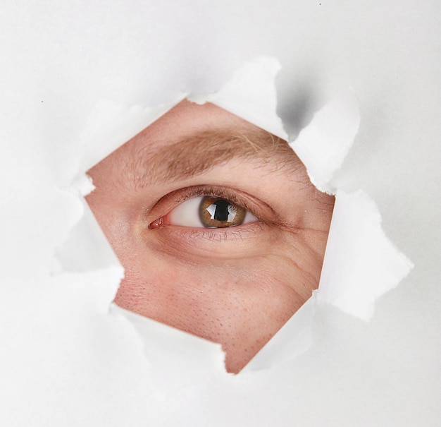 Photo oeil d'homme regardant à travers le trou d'une feuille de papier