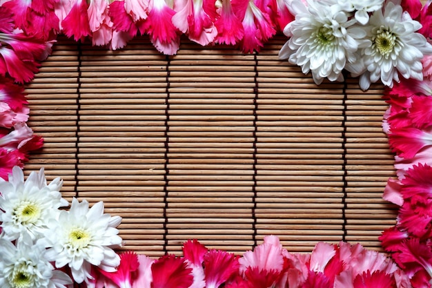 Oeillet rose et cadre de fleur blanche sur fond de natte de bambou.