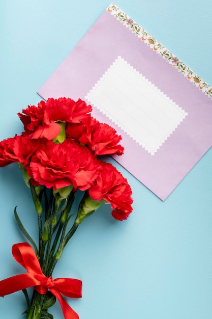 Oeillet rouge et enveloppe en papier rose avec un espace pour le texte sur la vue de dessus de fond bleu