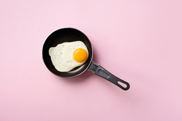 oeuf au plat sur une casserole sur fond rose