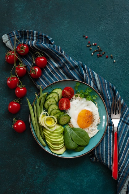 Oeuf au plat avec des légumes frais sur fond vert.