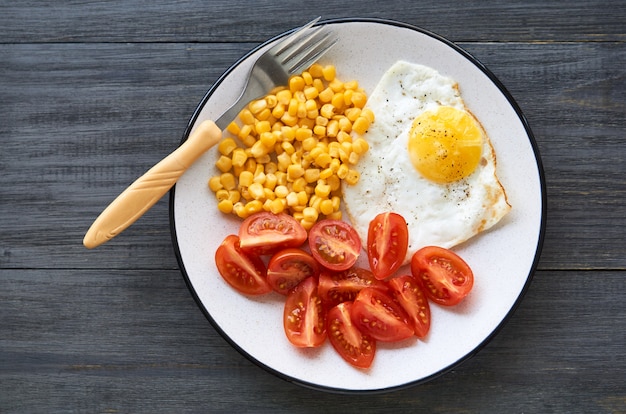 Oeuf au plat avec maïs et tomates sur une plaque grise