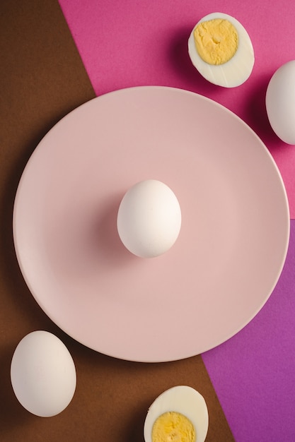 Oeuf blanc dans une assiette rose près d'œufs à la coque pelés sur pourpre