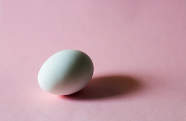 Oeuf blanc sur une table rose aux couleurs pastel.