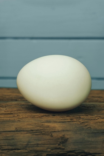 Un œuf blanc sur une vieille table en bois de chêne sur un fond bleu