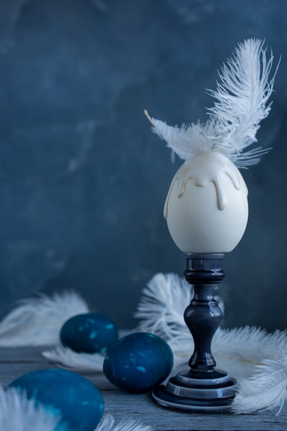 Oeuf en céramique blanche avec plume blanche sur un chandelier en céramique bleu.