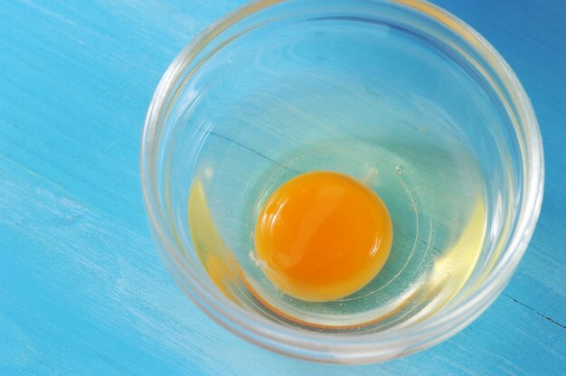 Oeuf cru dans un bol en verre sur un bleu