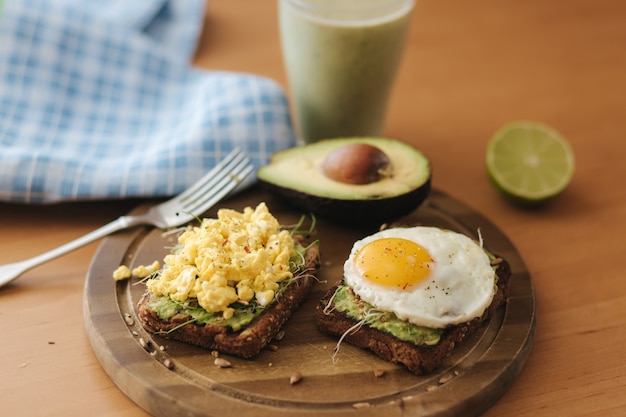 Oeuf cuit différent sur sandwich à l'avocat avec du pain de grains entiers sur planche de bois. Smoothie aux épinards.