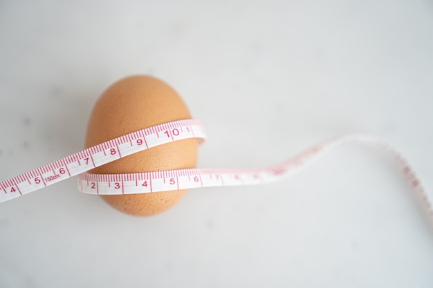 Oeuf enveloppé de ruban à mesurer sur une surface en marbre blanc