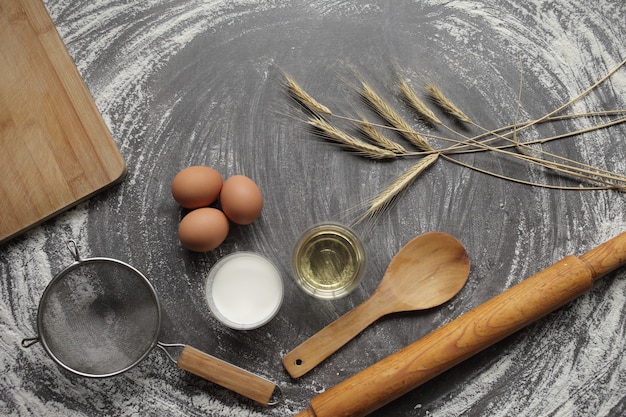 Oeuf, farine, huile d'olive, lait, épis de blé, outil de cuisine sur table grise