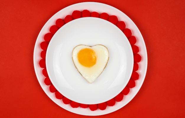 Oeuf en forme de coeur Petit-déjeuner de fête, déjeuner, Saint-Valentin. Sur une table rouge. Place pour votre texte.